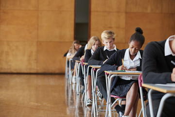 teenage students in uniform sitting examination in school hall