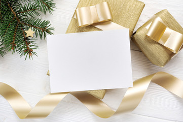 Mockup Christmas greeting card with gold gift ribbon, flatlay on a white wooden background, with place for your text