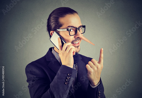 Valokuva Sly liar business man with long nose talking on mobile phone isolated on gray wall background