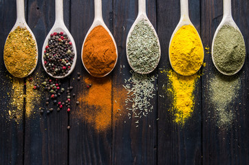 different spices in wooden spoons on a black wooden background