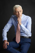 © gzorgz - Elderly man portrait. An executive senior man wearing shirt and tie while sitting at isolated black background.