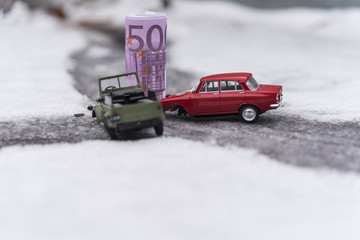 Toy cars and Euro crash on a slippery snowy road, the concept of spending money on auto repair.