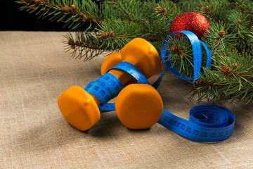 two orange dumbbells fitness Christmas tree with red new year ball and measuring tape for sports