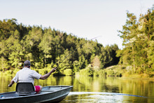 Rear View Of Man Fishing While Sitting In Rowboat On Lake Against Trees And Sky
