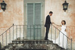 Wedding couple stands on the footsteps before an orange Italian villa