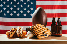 Beer Bottles With Hot Dogs And Sport Equipment With American Flag Behind