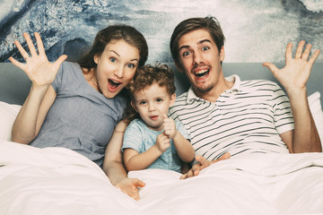 Wall Mural - Portrait of joyful young family lying in bed