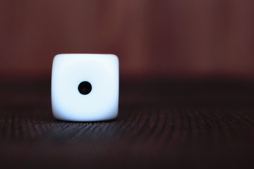 Wall Mural - Single white plastic dice on brown wooden board background. Six side cube with black dots. Number 1.