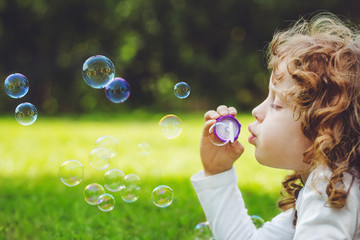 Sticker - little girl blowing soap bubbles in summer park.