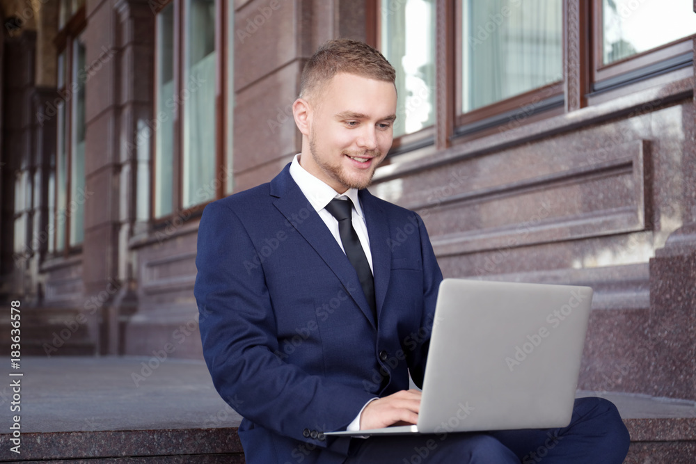 Handsome businessman working with laptop while sitting on stairs outdoors