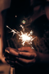 Wall Mural - hand holding a burning sparkler firework bengal light. space for text. burning sparkler closeup in female hand in dark. happy new year and merry christmas concept. happy holidays