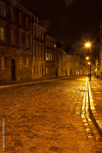 Plakat Ulica Mostowa w Warszawie w godzinach wieczornych z latarniami w kolorach pomarańczowych