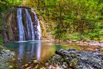 Waterfall in a green spring forest surrounded by stones, clear turquoise water on an impressive natural landscape. 33 Waterfalls, Sochi, Russia.