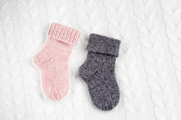 A pair of cute small different colored cashmere knitted newborn baby socks on a white woolen background