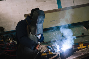 Manufacture worker welding metal at factory workshop with flying sparks