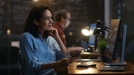 Poster - Beautiful Female Financier Uses Mobile Phone, Writing Messages, Emails while Smiling.In the Background Creative Office with Employees. RED EPIC-W 8K Camera.