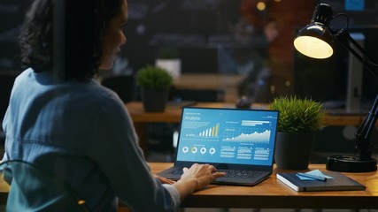 Poster - Female Analyst at Her Desk Works on a Laptop Showing Statistics, Graphs and Charts. She Works on the Wooden Table in Creative Office. Over the Shoulder Footage. RED EPIC-W 8K Camera.
