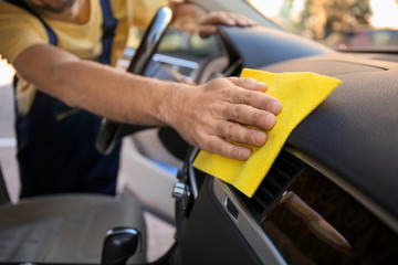 Man cleaning car dashboard with rag, closeup