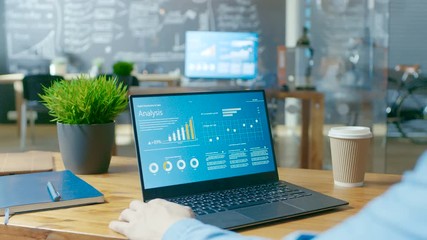 Poster - Male Analyst at His Desk Works on a Laptop Showing Statistics, Graphs and Charts. He Works in Light and Modern Creative Office.RED EPIC-W 8K Camera.