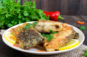 Wall Mural - Pieces of roasted carp with lemon and greens on a plate on a dark wooden background.