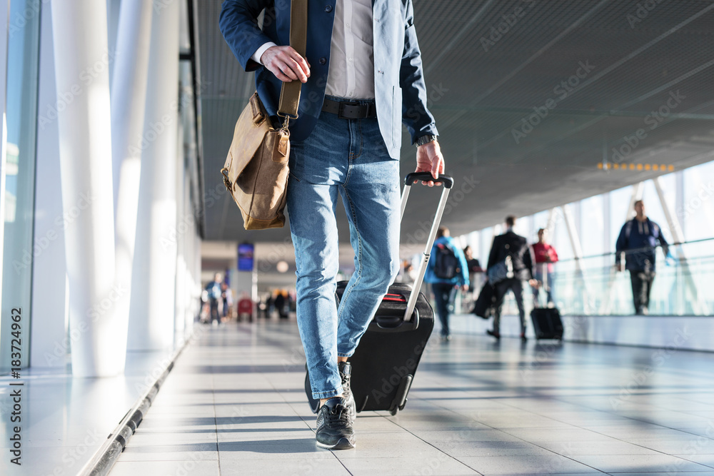 Man with shoulder bag and hand luggage walking in airport terminal - obrazy, fototapety, plakaty 
