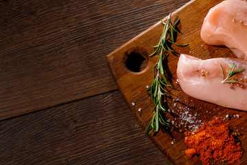 Raw chicken breast, pepper, rosemary on a cutting board, on a wooden background, close-up. Raw chicken meat for cooking. Delicious balanced nutrition concept. Copy space