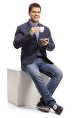 Poster - Elegant guy sitting on a cube and holding a cup