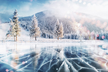 Wall Mural - Blue ice and cracks on the surface of the ice. Frozen lake in winter mountains. It is snowing. The hills of pines. Winter. Carpathian Ukraine Europe