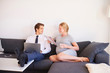 © Connect Images - Pregnant couple sitting on sofa with magazine and laptop