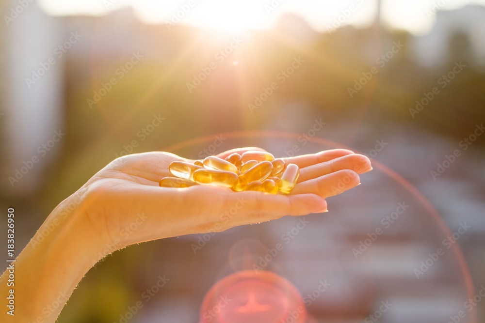 Obraz na płótnie Hand of a woman holding fish oil Omega-3 capsules, urban sunset background. Healthy eating, medicine, health care, food supplements and people concept w salonie