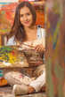 Beautiful young woman painter sitting in the floor with color palette and paint brush in hand, in a blurred background