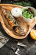 Beautiful grilled fish with lemon on a wooden plate with a glass of white wine on a dark wooden background