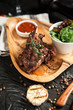 baked lamb on bone with tomato sauce, salad on a wooden plate with a glass of red wine on a dark wooden background