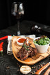 baked lamb on bone with tomato sauce, salad on a wooden plate with a glass of red wine on a dark wooden background