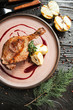 beautiful serving duck leg confit with apples and berry sauce on a wooden plate with a glass of red wine