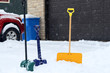 Beautiful winter background. Three colorful shovels in snowdrift on a foreground along covered by fresh snow driveway and garage door on a snowy background.