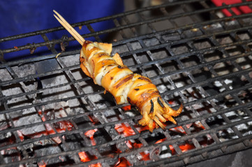 Grilled squid on a stick roasted on the fire  at street food of Thailand.