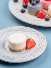 Wall Mural - Small round berry cheesecakes on plate and blue background