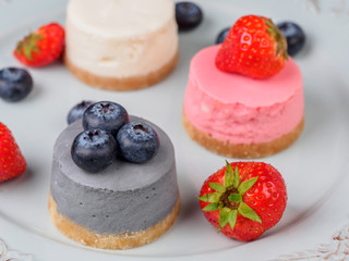 Wall Mural - Small round berry cheesecakes on plate and blue background