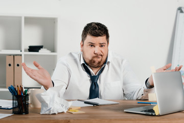 Wall Mural - confused overweight businessman sitting at workspace with documents and laptop