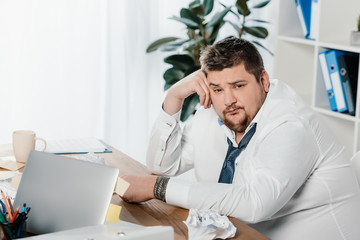 Wall Mural - fat businessman sitting at workplace with crumpled papers and laptop