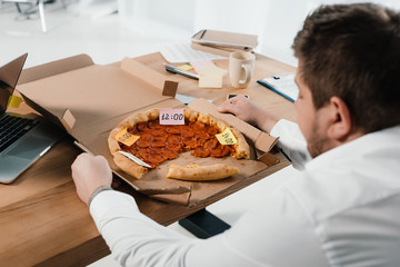 Wall Mural - overweight businessman eating pizza at workplace in office