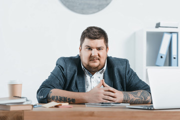 Wall Mural - confident overweight businessman sitting at workplace in office