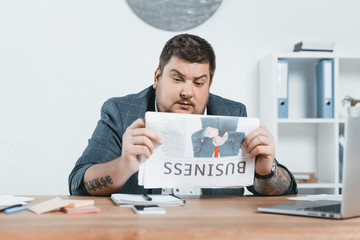 Wall Mural - overweight businessman in suit reading business newspaper at workplace