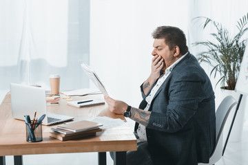 Wall Mural - overweight yawning businessman in suit reading newspaper at workplace