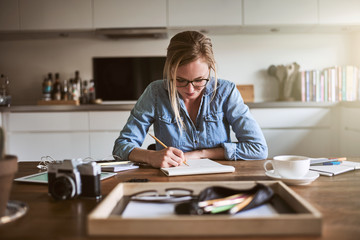 Wall Mural - Young woman working from home and sketching on a notepad