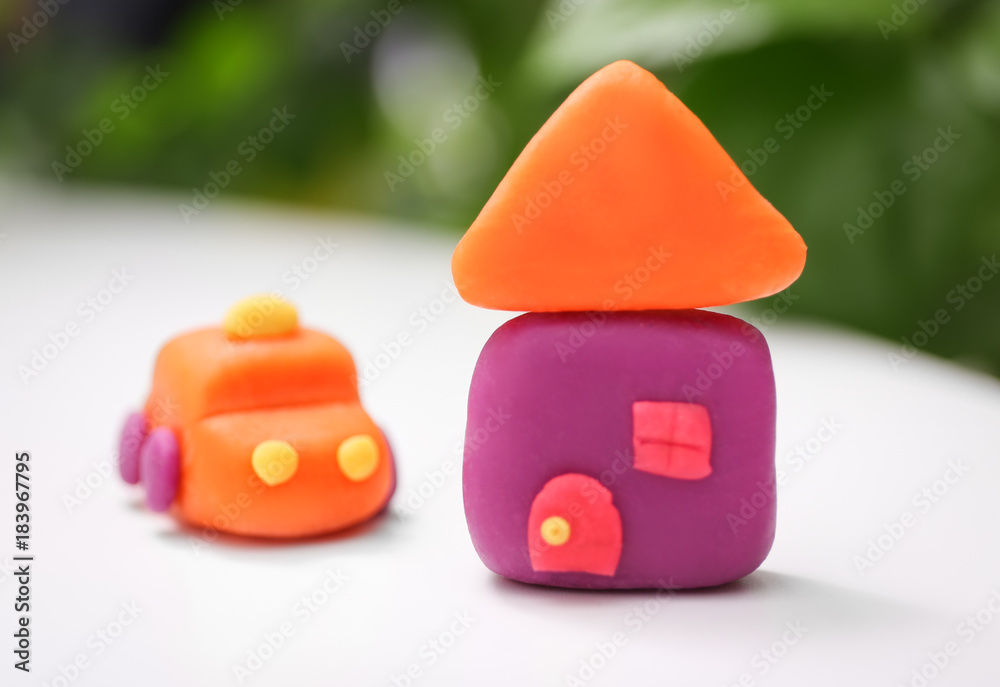Car and house made from playdough on table against blurred background, closeup