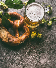 Close up of mug of beer and pretzel with hops on dark rustic background, top view, copy space. German style