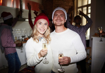 Poster - Happy young couple in white sweaters holding flutes with champagne at party