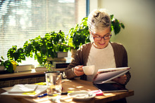 Charming Cheerful Satisfied Middle Age Short Hair Woman Sitting At The Table In The Morning At Home And Drinking A Coffee While Reading Students Tests Or Business Statistics.